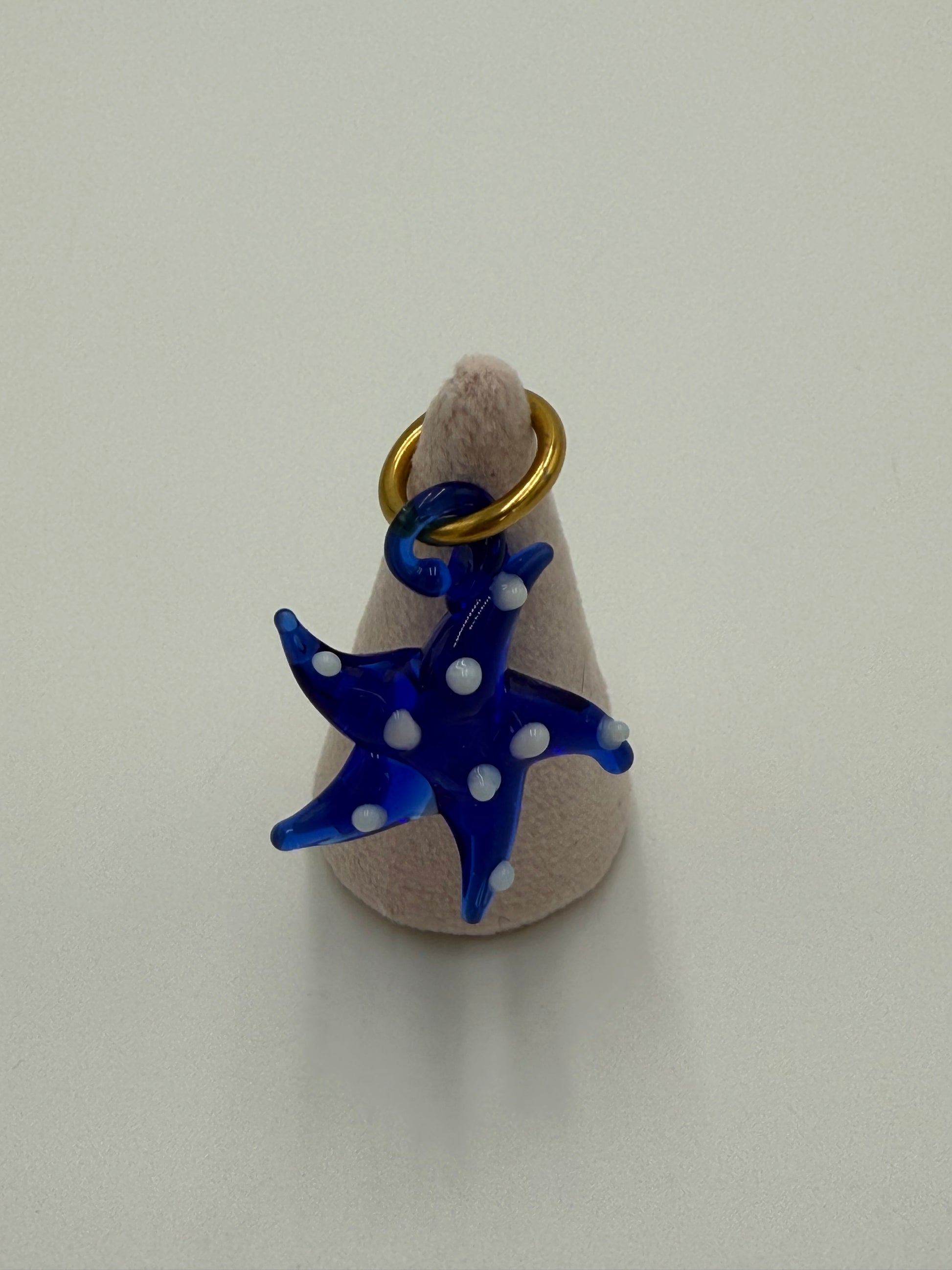 Handgemaakte blauwe glazen zeester kettingbedel met witte stippen, bevestigd aan een bronzen ring verguld met 24 karaat goud
