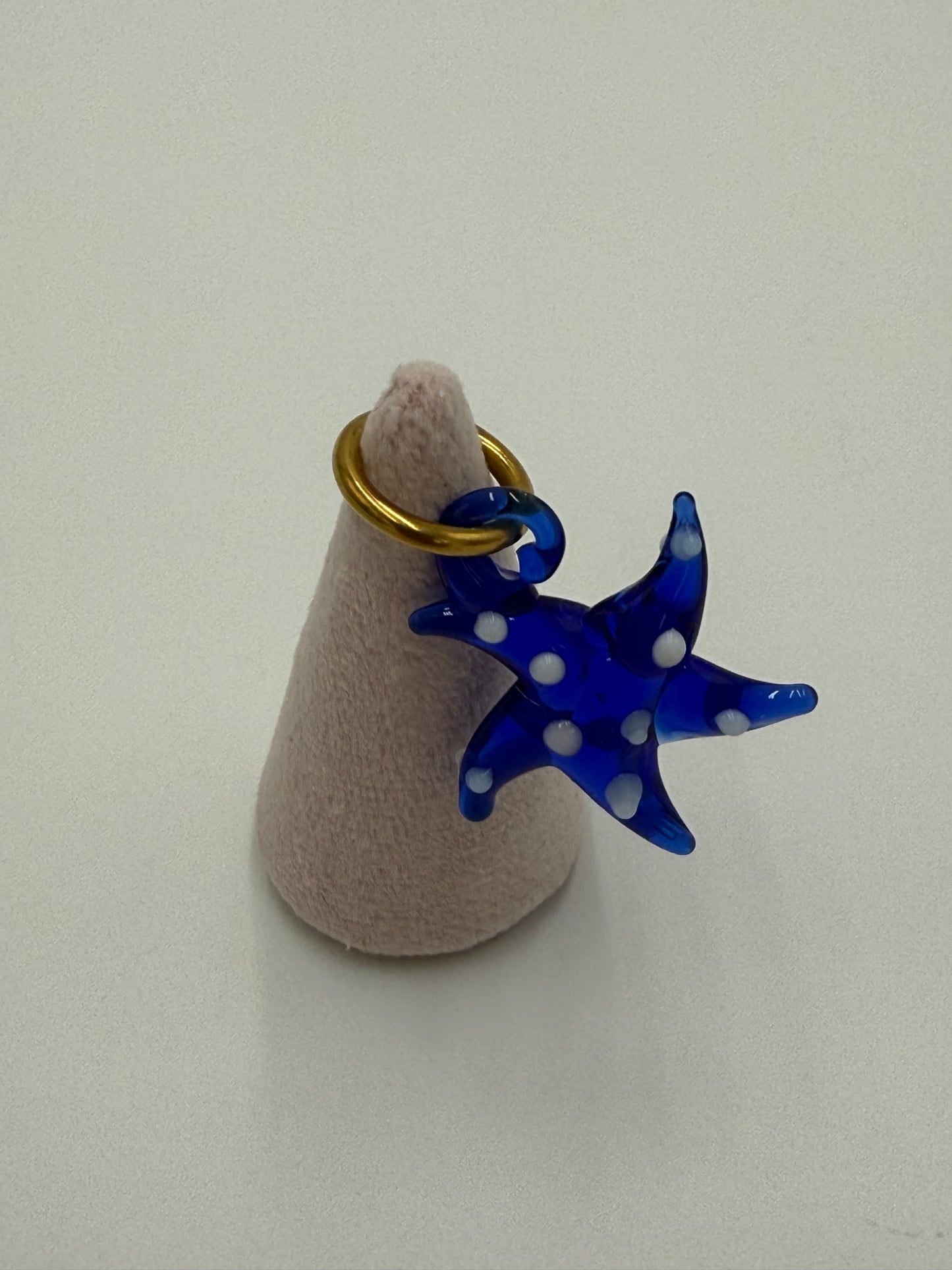 Handgemaakte blauwe glazen zeester kettingbedel met witte stippen in transparant glas, hangend aan een bronzen ring verguld met 24 karaat goud