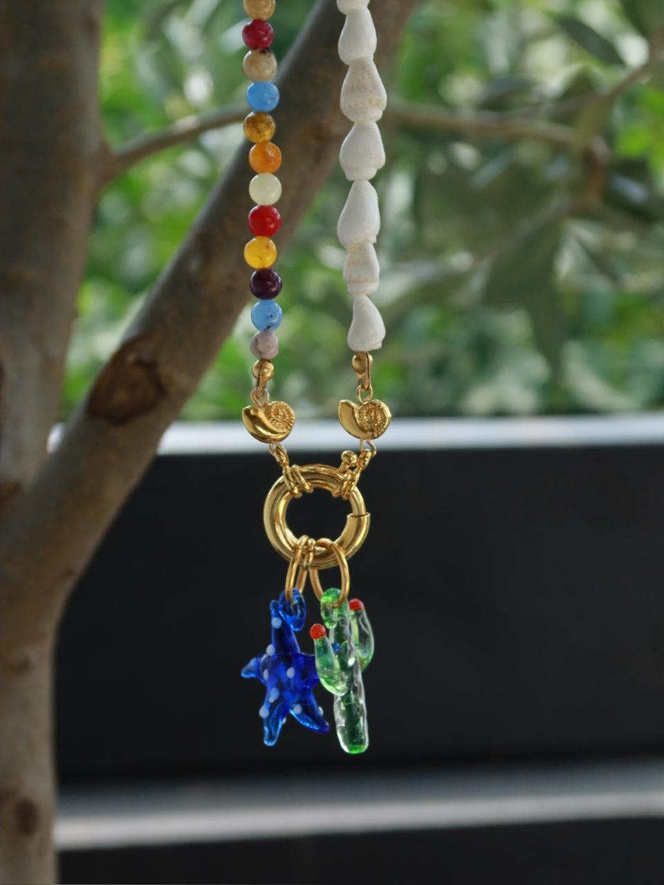 Handgemaakte glazen zeester kettingbedel in blauw met witte stippen, gecombineerd met andere bedels aan een kleurrijke ketting met vergulde bronzen sluiting