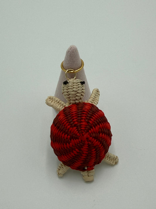 Handgemaakte schildpad kettingbedel van gevlochten Werregué-palm met rood schild en natuurlijke tinten, afgewerkt met een bronzen ring verguld met 24 karaat goud