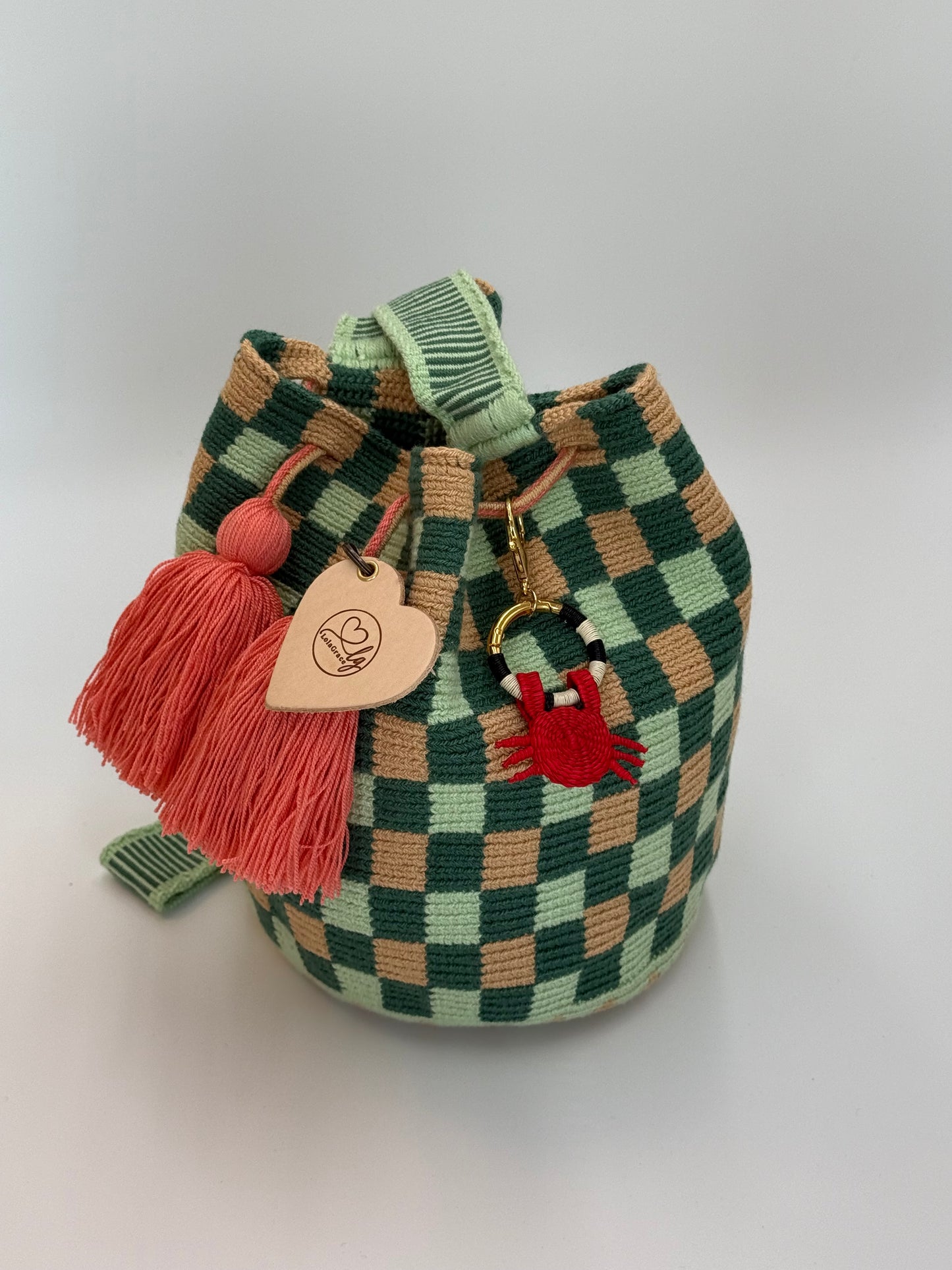 Handgemaakte LolaGrace krab tasbedel van Werregue-palm met brons en 24-karaat vergulde details bevestigd aan een Wayuu mochila tas.