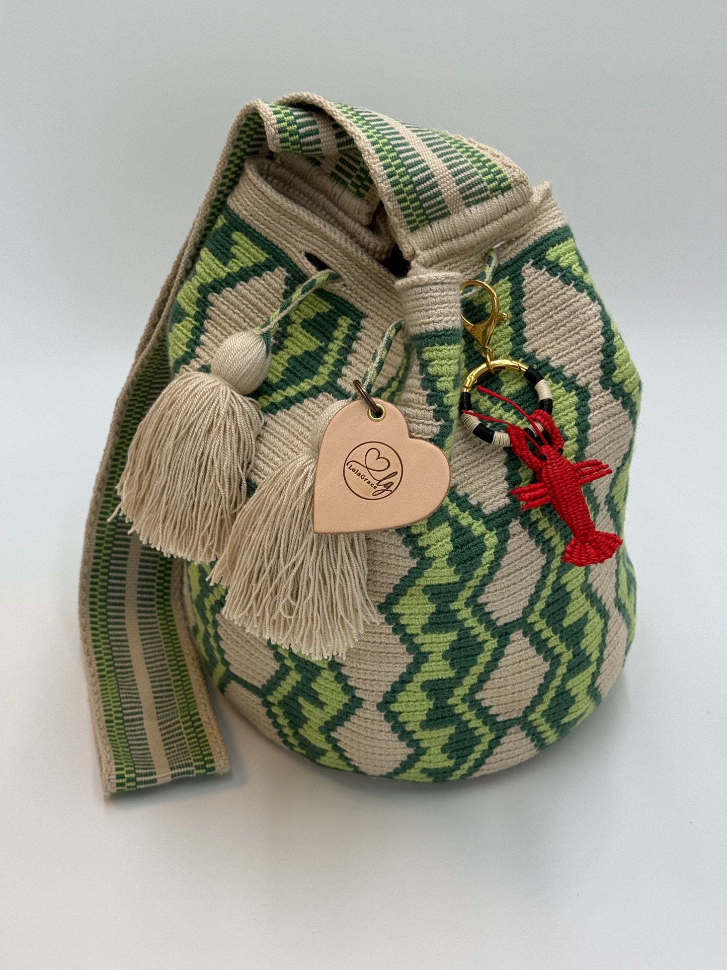 Handgemaakte LolaGrace kreeft tasbedel van Werregue-palm met brons en 24-karaat vergulde details bevestigd aan een Wayuu mochila tas.