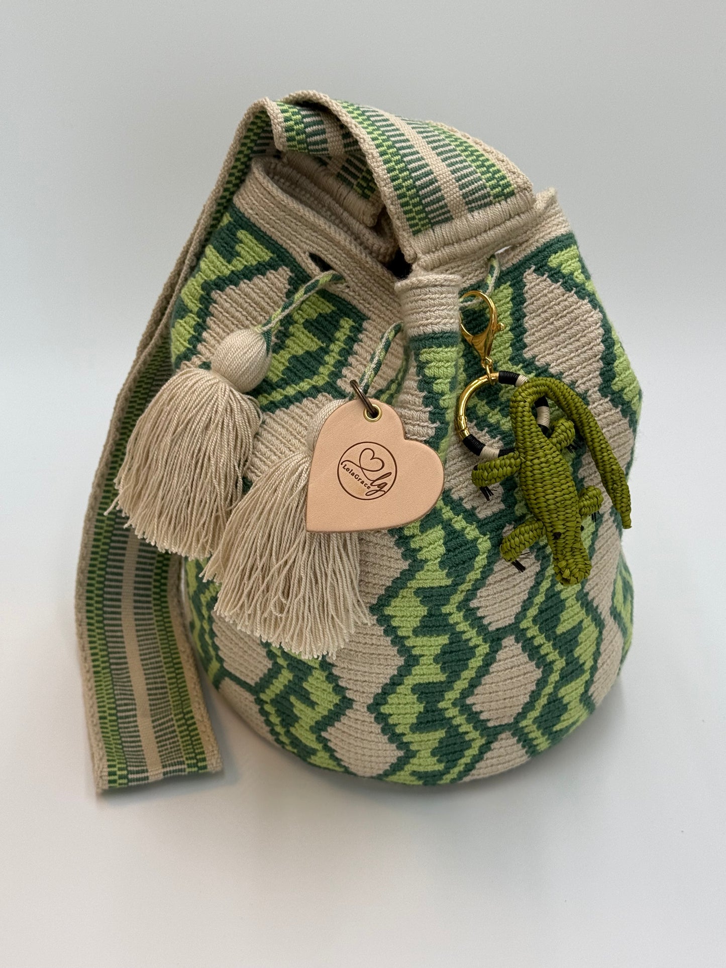 Handgemaakte LolaGrace krokodil tasbedel van Werregue-palm met brons en 24-karaat vergulde details bevestigd aan een Wayuu mochila tas.