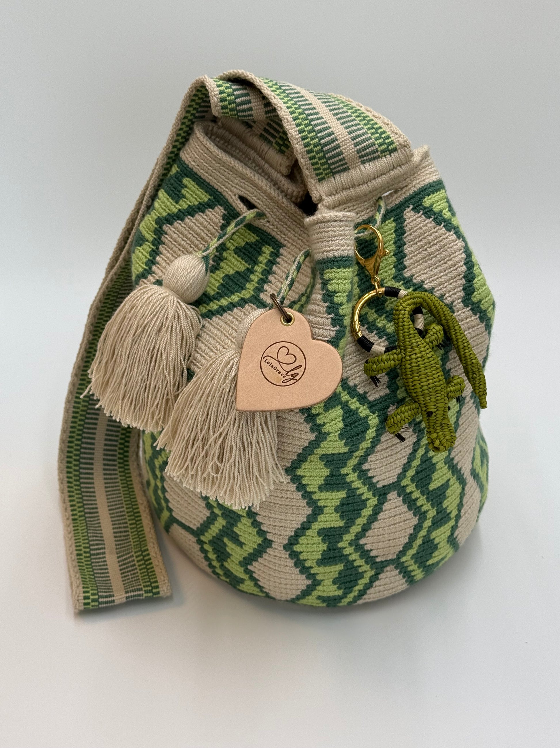 Handgemaakte LolaGrace krokodil tasbedel van Werregue-palm met brons en 24-karaat vergulde details bevestigd aan een Wayuu mochila tas.