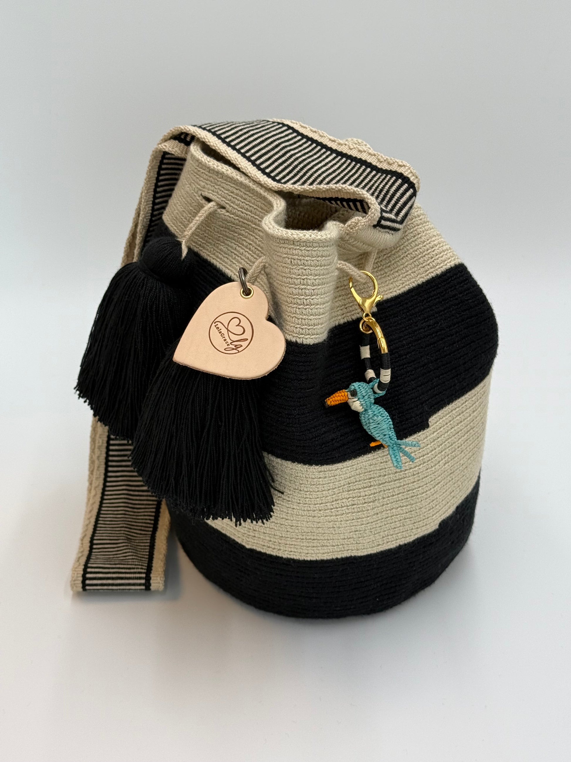 Handgemaakte LolaGrace blauwe vogel tasbedel van Werregue-palm met brons en 24-karaat vergulde details bevestigd aan een Wayuu mochila tas.