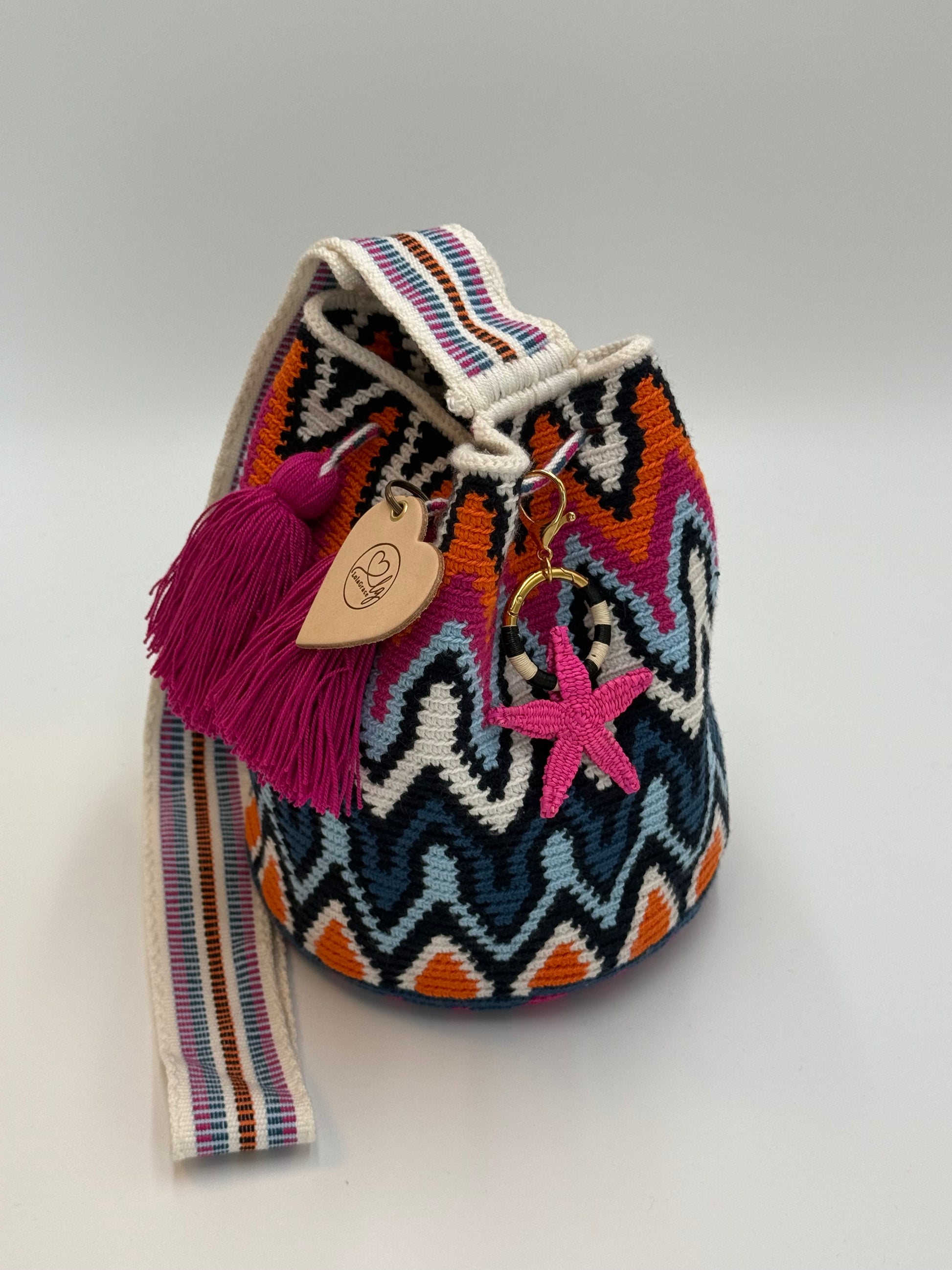 Handgemaakte LolaGrace zeester tasbedel van Werregue-palm met brons en 24-karaat vergulde details bevestigd aan een Wayuu mochila tas.