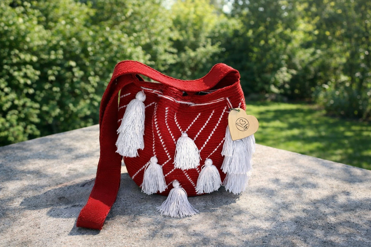 Ana Sofía medium Wayuu tas van LolaGrace handgemaakt in Colombia met rood patroon en witte kwasten op stenen tafel in natuurlijke omgeving