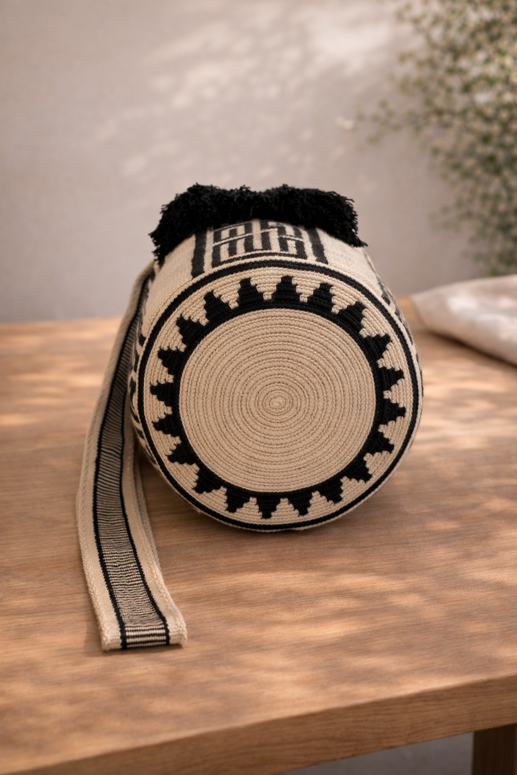 Angie Medium Wayuu mochila tas van LolaGrace op houten tafel, handgemaakt in Colombia met crème en zwart geometrisch patroon.