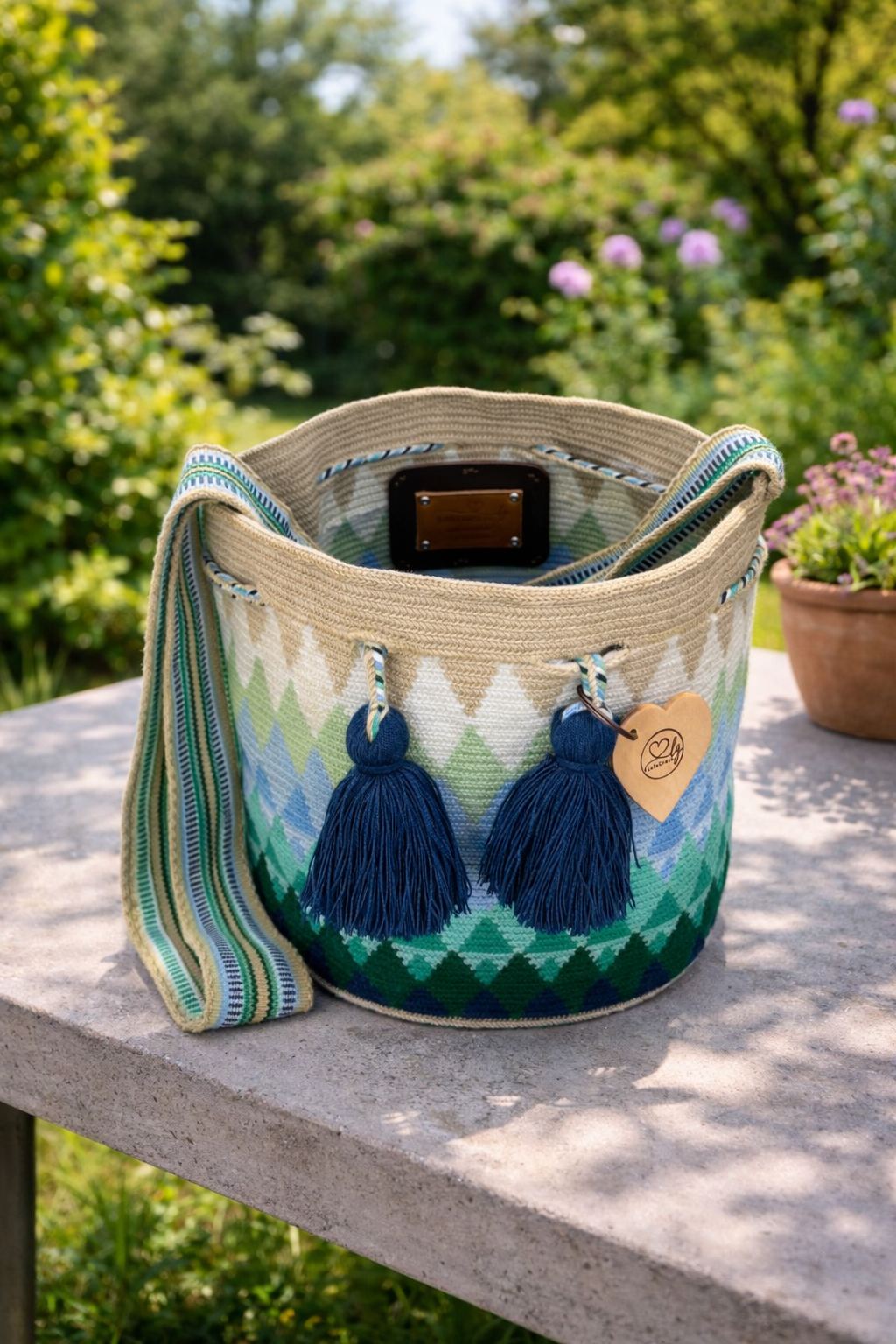 Danna large Wayuu mochila tas van LolaGrace handgemaakt in Colombia met groen en blauw geometrisch patroon en donkerblauwe kwasten op stenen tafel in tuin