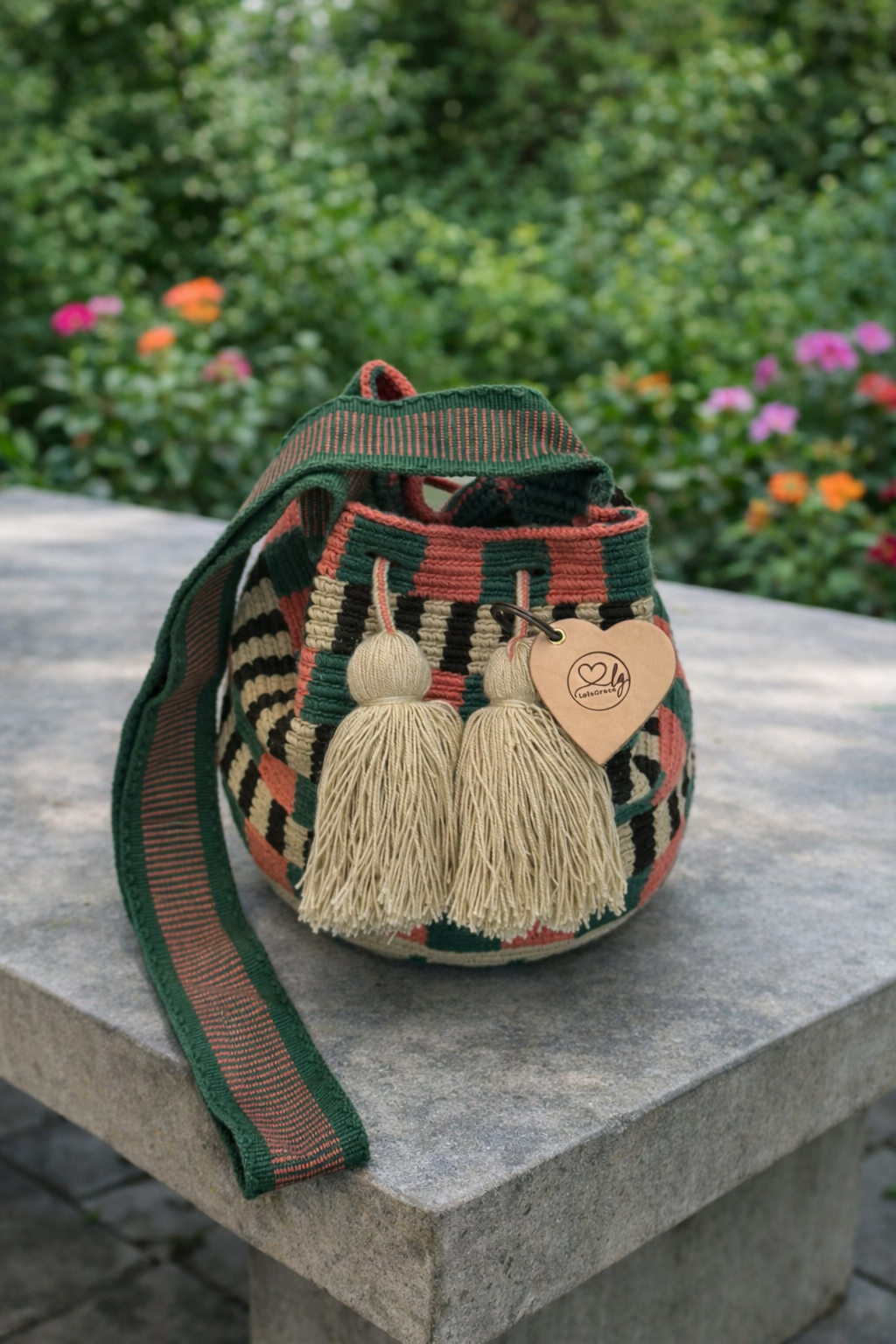 Handgemaakte medium Wayuu tas Eliana met groen-roze patroon en beige kwastjes op betonnen tafel in buitenomgeving