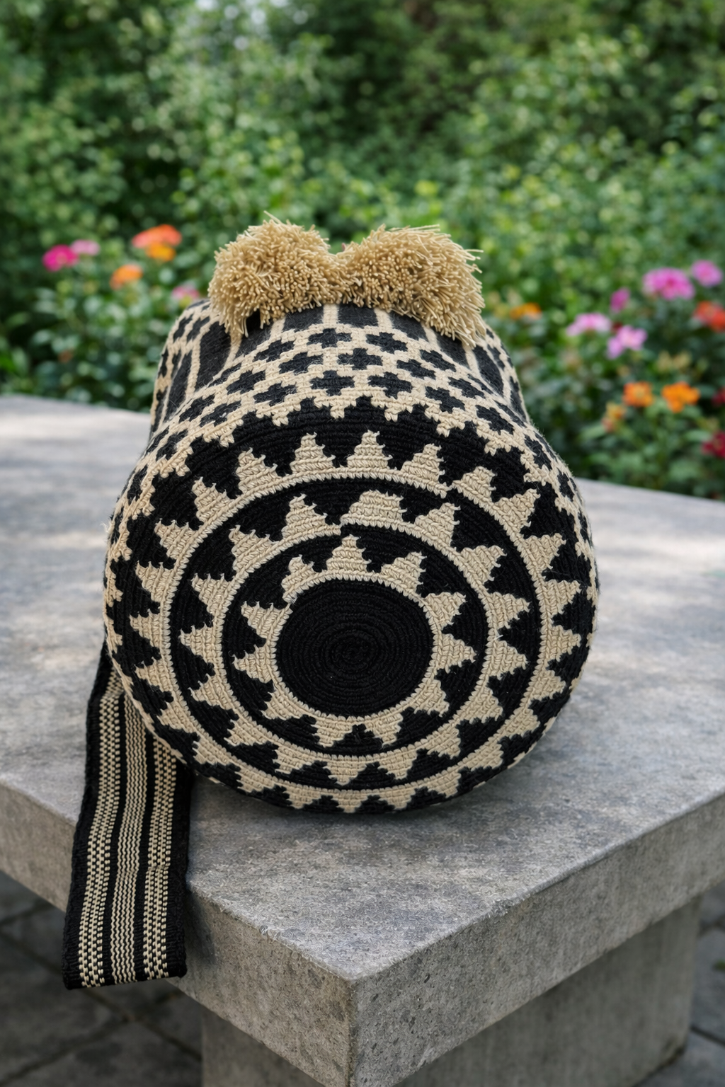 Handgemaakte large Wayuu tas Gloria met zwart-crème patroon en beige kwastjes op betonnen tafel in buitenomgeving