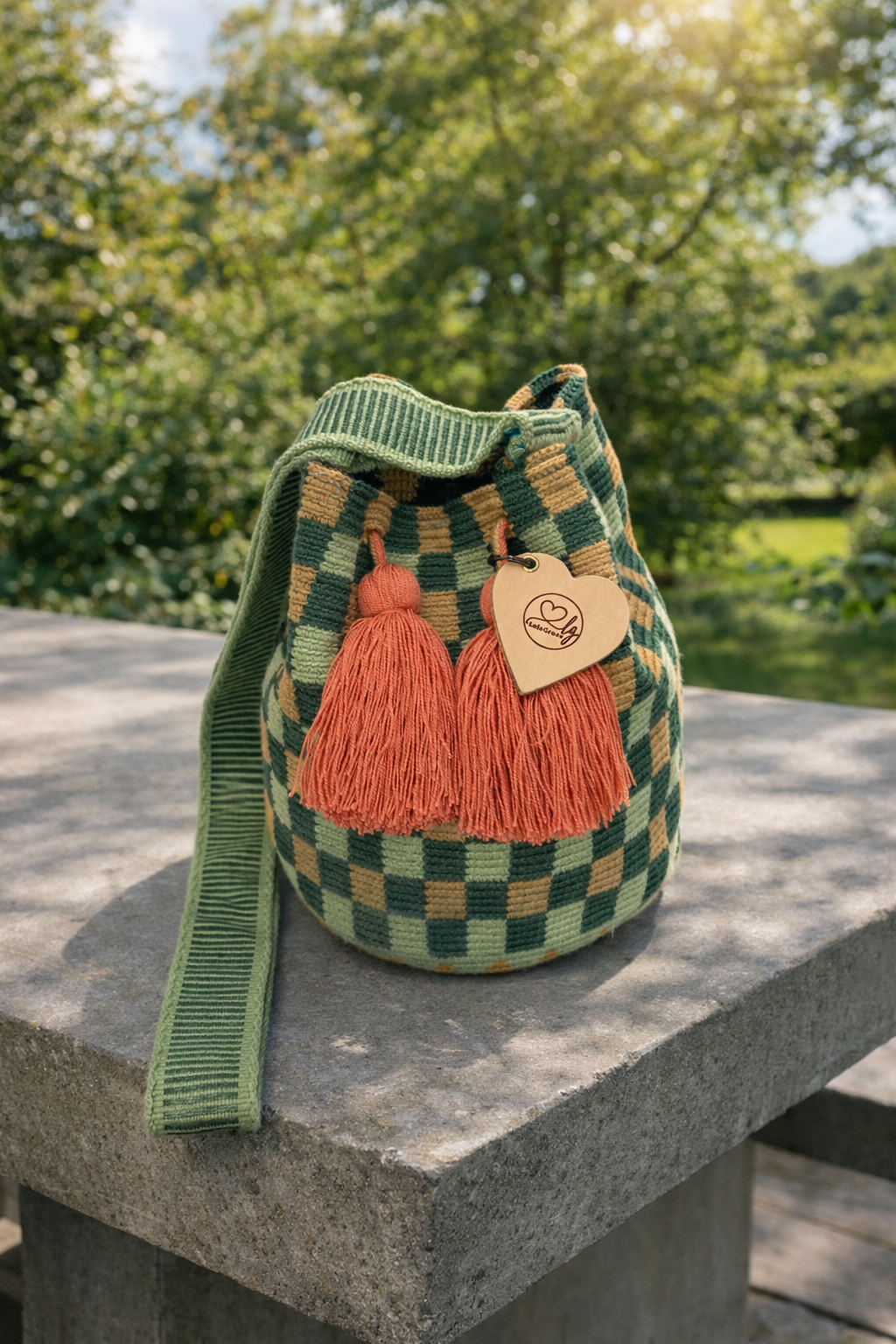 Julieta medium Wayuu tas van LolaGrace handgemaakt in Colombia met groen patroon en roze kwasten op stenen tafel in natuurlijke omgeving