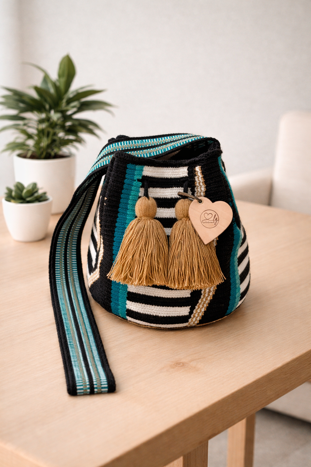 Kelly medium Wayuu tas van LolaGrace handgemaakt in Colombia met zwart patroon en turquoise strepen op houten tafel in interieur