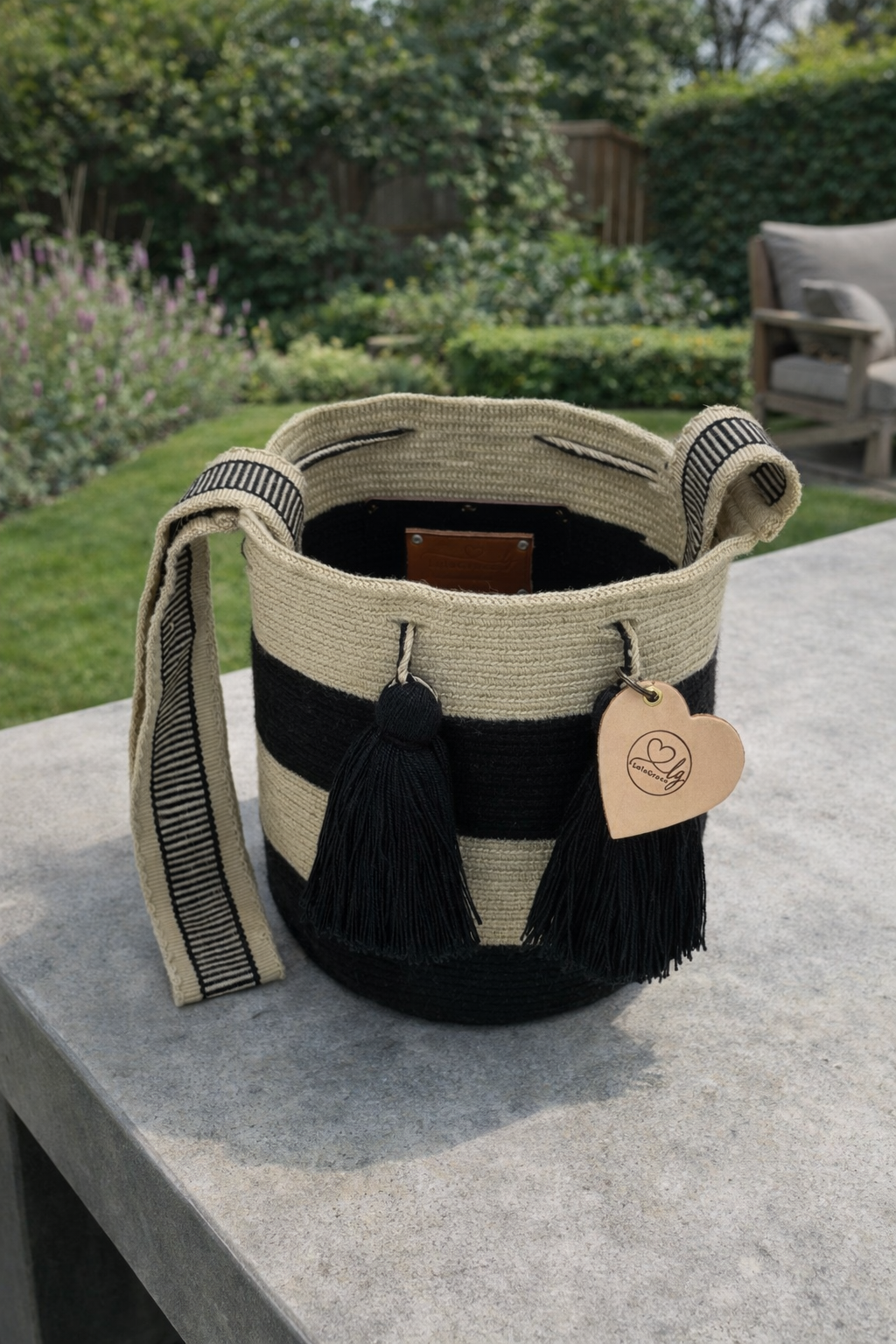 Open handgemaakte Luna Medium Wayuu tas van LolaGrace in zwart en crème op betonnen tafel met natuurlijke tuinachtergrond.