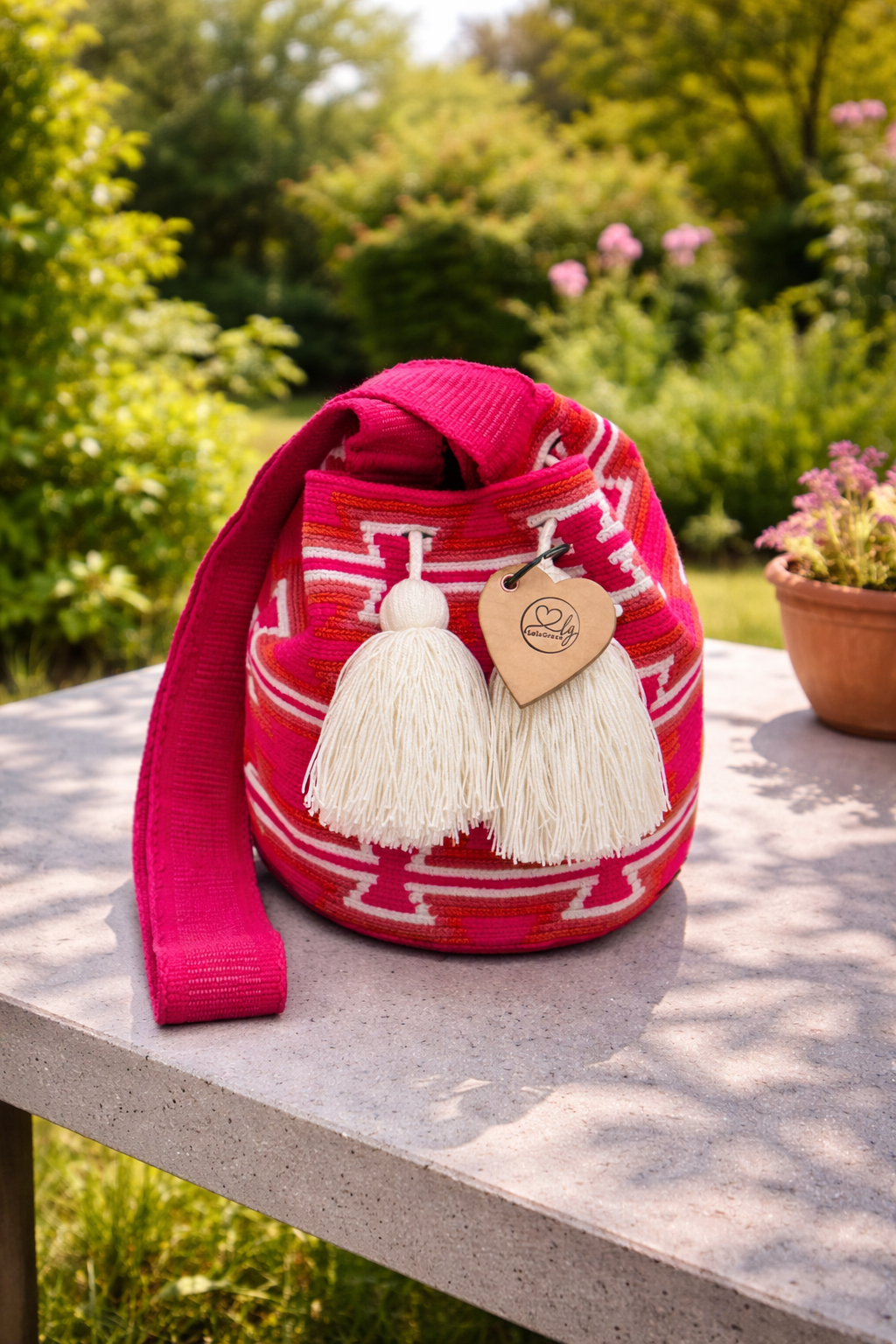 María Fernanda medium Wayuu tas van LolaGrace handgemaakt in Colombia met fuchsia roze patroon en witte kwasten op stenen tafel in tuin