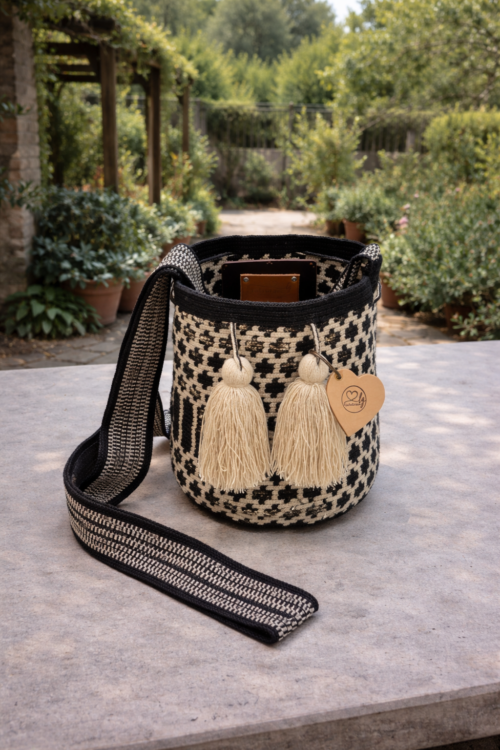 Ambachtelijke medium Wayuu tas Miriam in zwart en crème op een tafel in een groene, rustige buitenomgeving
