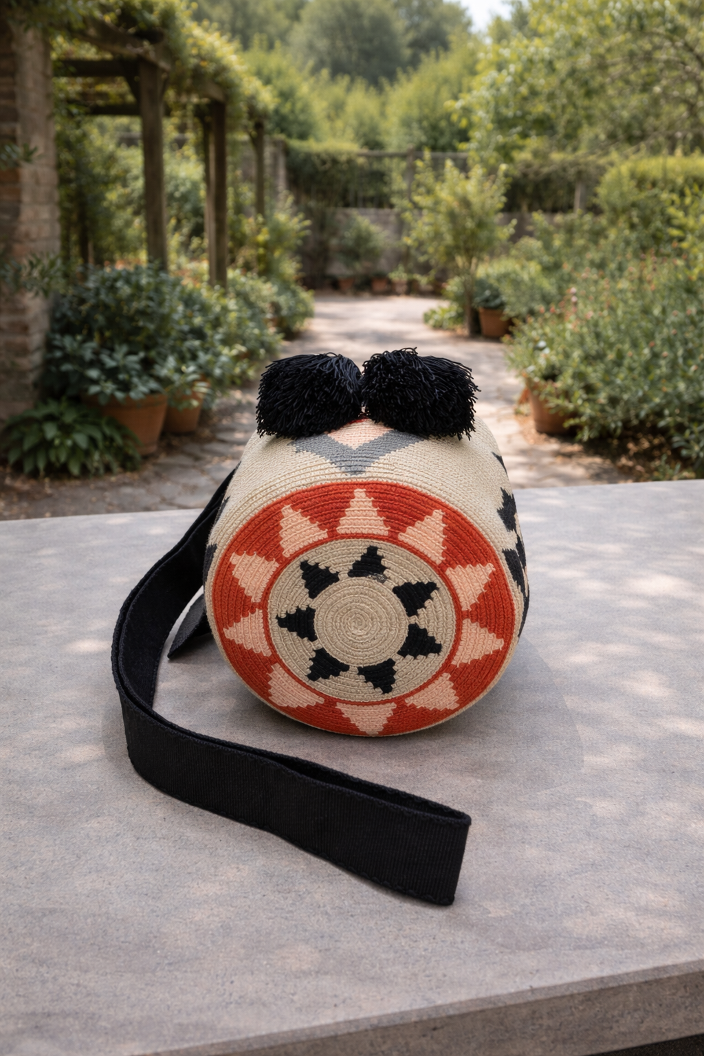 Handgeweven Wayuu tas Nayibe met grafisch design in natuurlijke en warme tinten, geplaatst in een rustige tuinsetting