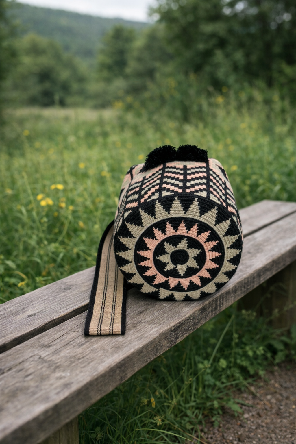 Handgemaakte Wayuu tas Olga Large van LolaGrace met traditioneel zwart-crème patroon op houten bank in natuurlijke omgeving.