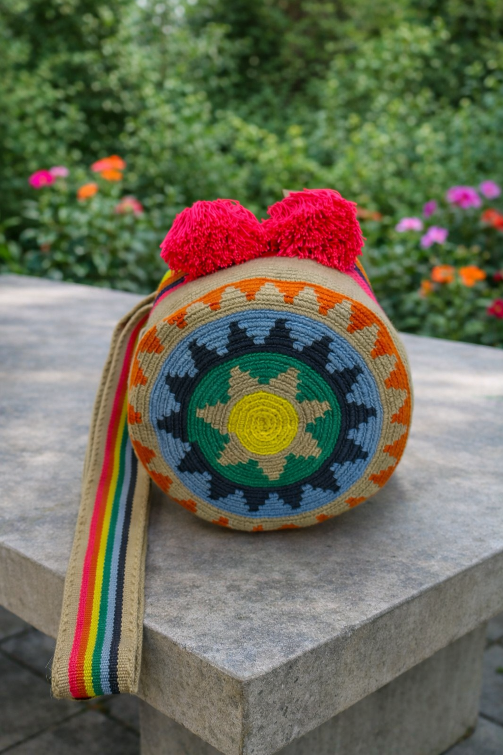 Handgemaakte medium Wayuu tas Samanta met kleurrijk patroon en roze kwastjes op betonnen tafel in buitenomgeving