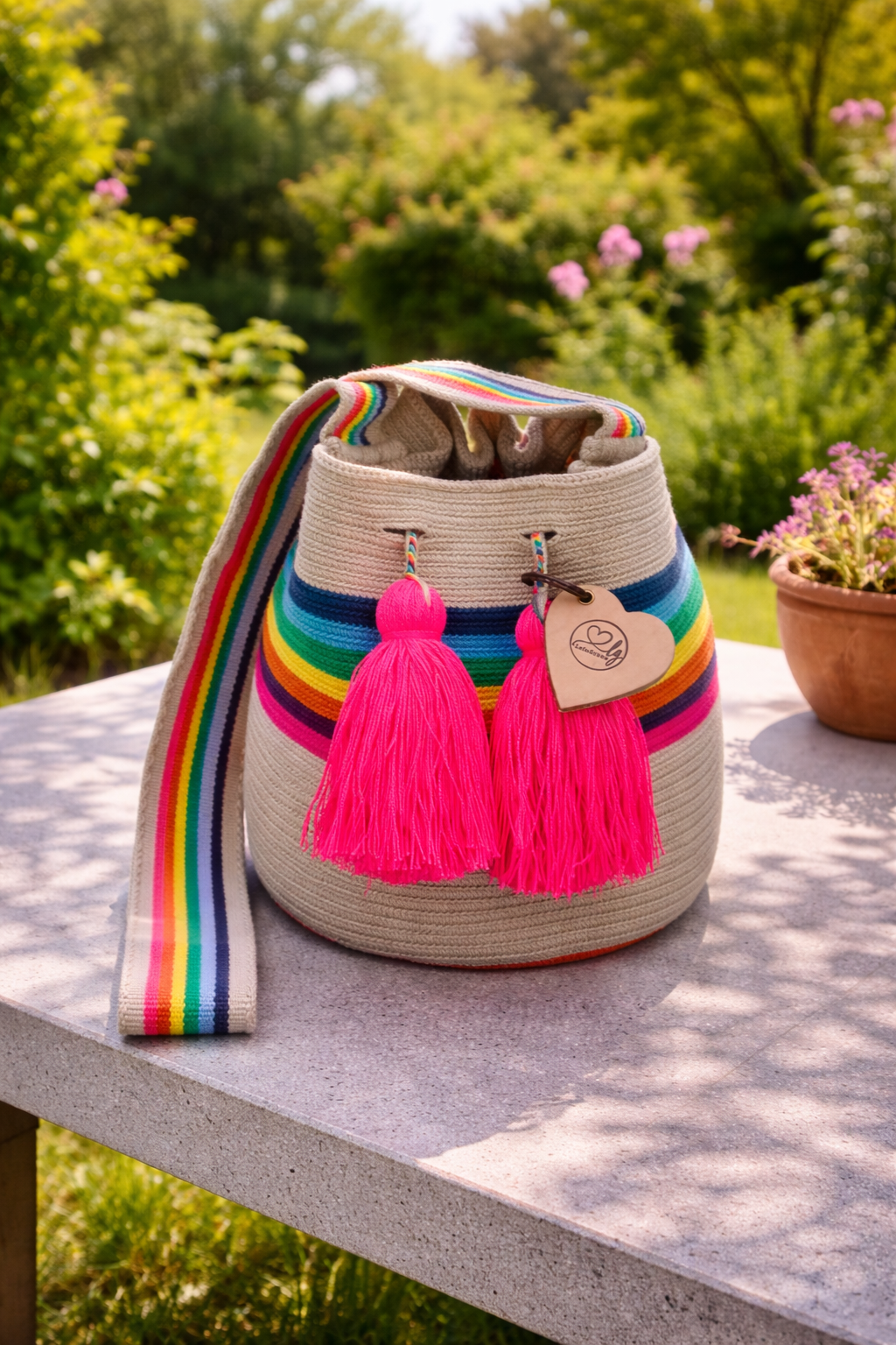 Sara Lucia medium Wayuu tas van LolaGrace handgemaakt in Colombia met regenboog strepen en neon roze kwasten op stenen tafel in tuin