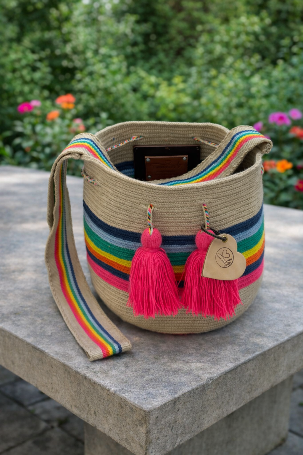 Handgemaakte large Wayuu tas Sofía Andrea met kleurrijk patroon en roze kwastjes op betonnen tafel in buitenomgeving