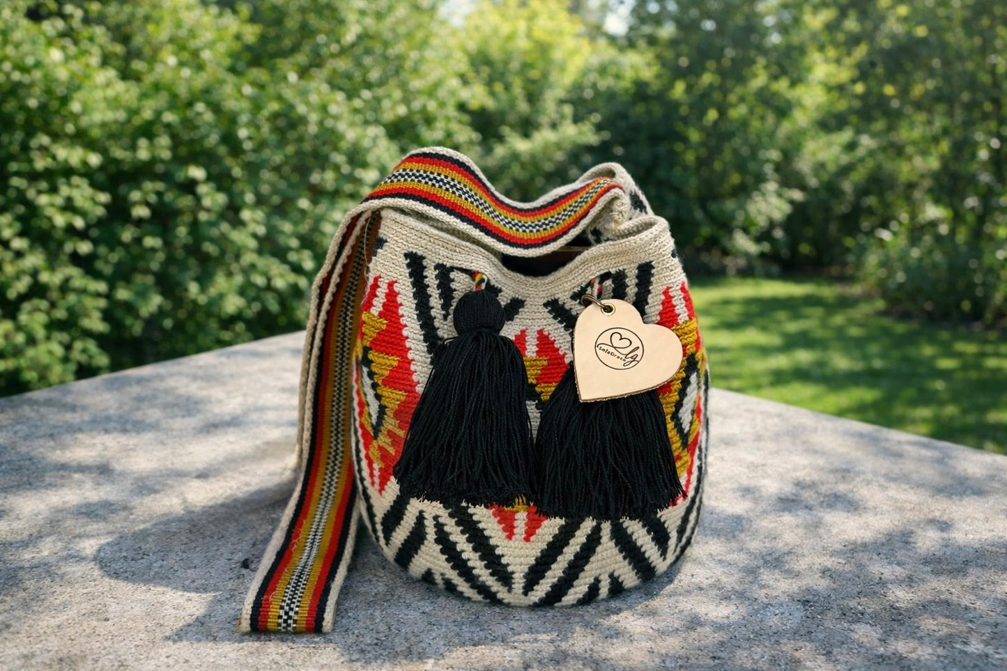 Valentina María medium Wayuu tas van LolaGrace handgemaakt in Colombia met zwart-wit patroon rode details en zwarte kwasten op stenen tafel in natuurlijke omgeving