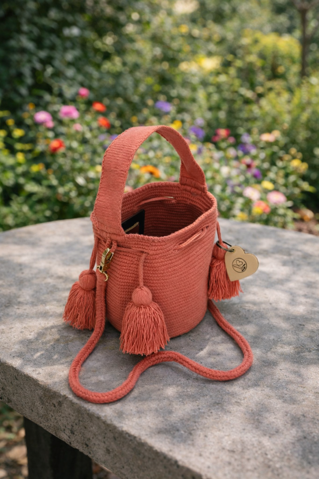 Vrouwelijke Wayuu tas Xiomara in warme koraaltint, stijlvol gepresenteerd in een zonnige tuinsetting