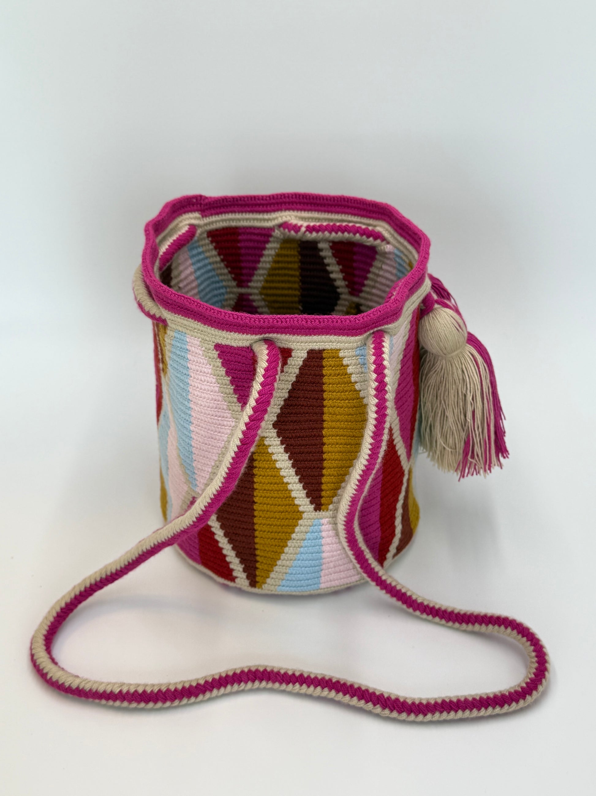 Zijkant van Wayuu tas Ines Medium van LolaGrace met kleurrijk geometrisch patroon in roze, crème, oker en lichtblauw en een handgeweven schouderband.