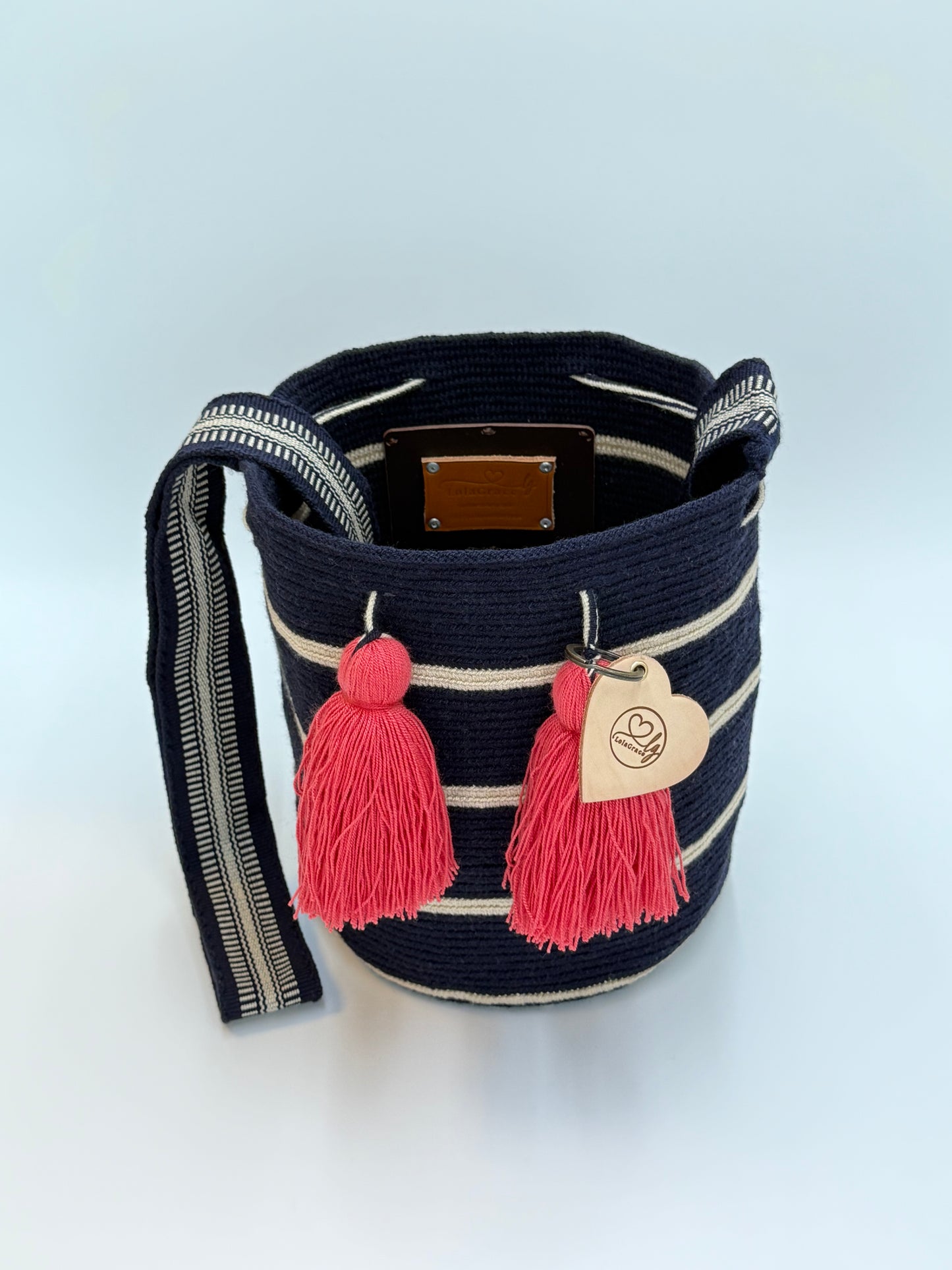 Open Melany Medium Wayuu mochila tas van LolaGrace van bovenaf met handgehaakte structuur, donkerblauw en beige strepen en roze kwasten.