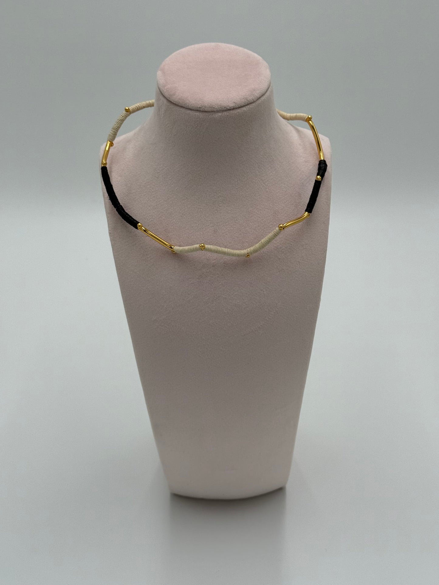 Handgemaakte Barichara choker van LolaGrace met verguld brons en natuurlijke Werregué palmvezel in zwart en beige tinten, gepresenteerd op een sieradenstandaard.