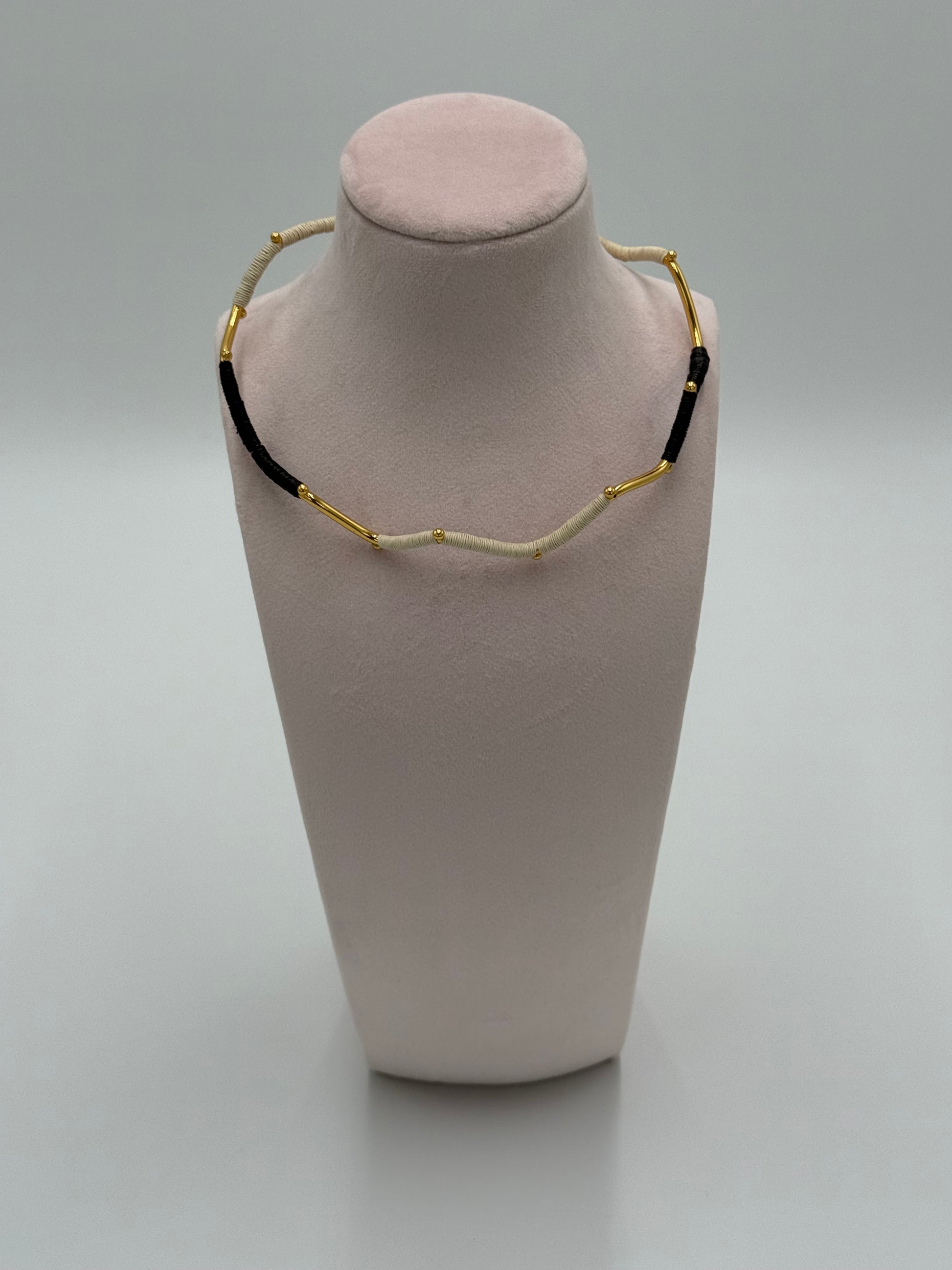 Handgemaakte Barichara choker van LolaGrace met verguld brons en natuurlijke Werregué palmvezel in zwart en beige tinten, gepresenteerd op een sieradenstandaard.