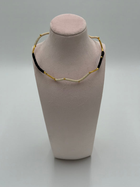 Handgemaakte Barichara choker van LolaGrace met verguld brons en natuurlijke Werregué palmvezel in zwart en beige tinten, gepresenteerd op een sieradenstandaard.