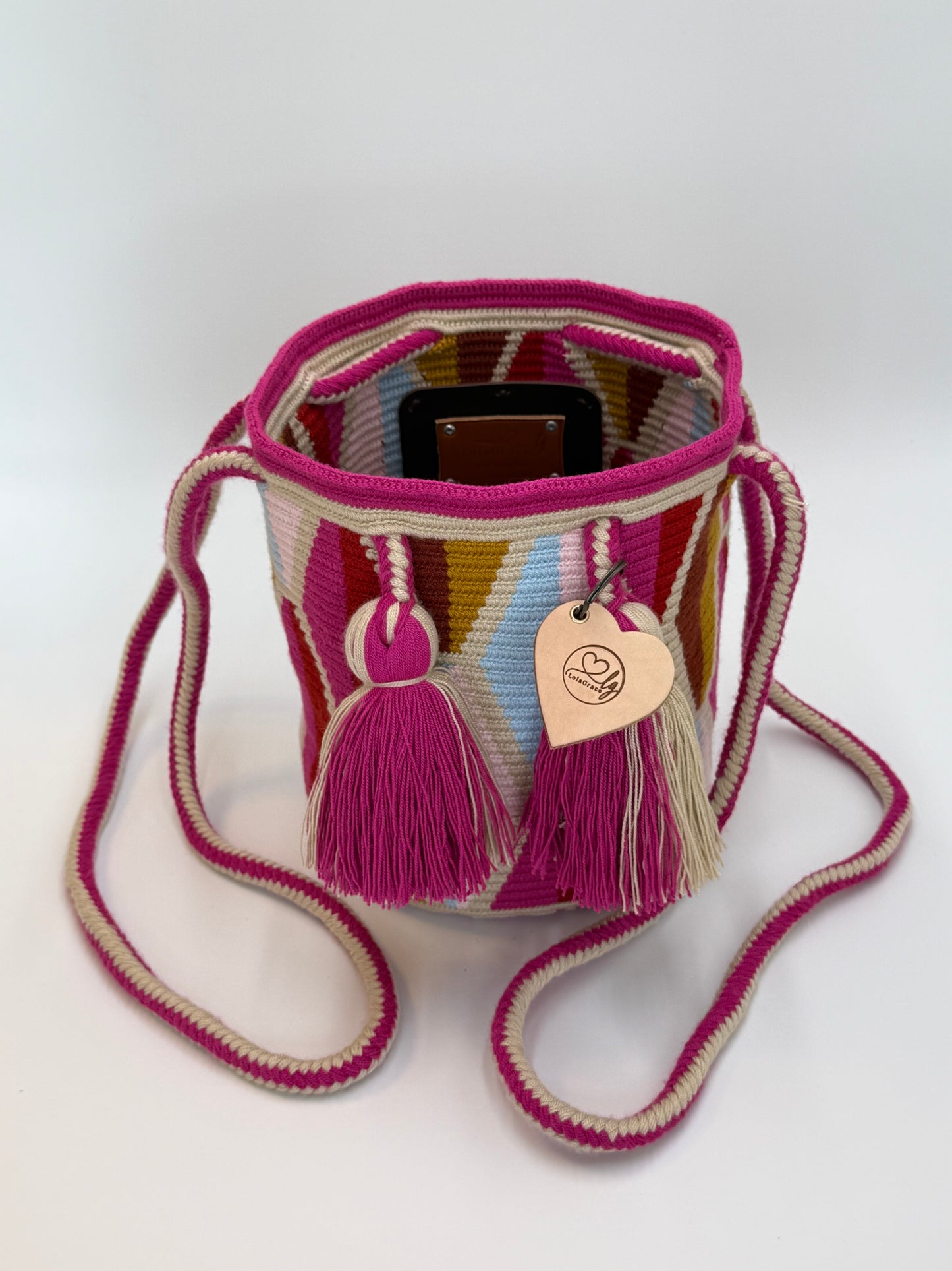 Voorkant van handgemaakte Wayuu tas Ines Medium van LolaGrace met roze en beige kwastjes, trekkoordsluiting en kleurrijk traditioneel Wayuu patroon.