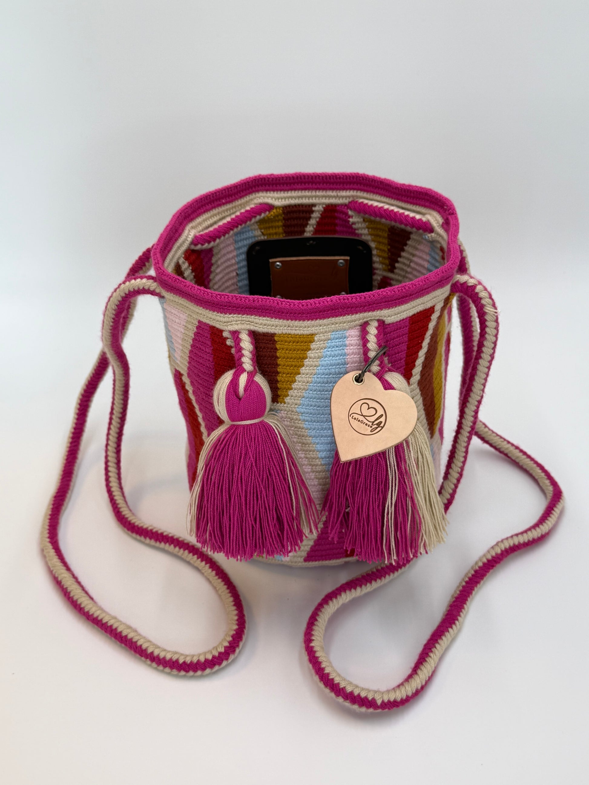 Voorkant van handgemaakte Wayuu tas Ines Medium van LolaGrace met roze en beige kwastjes, trekkoordsluiting en kleurrijk traditioneel Wayuu patroon.