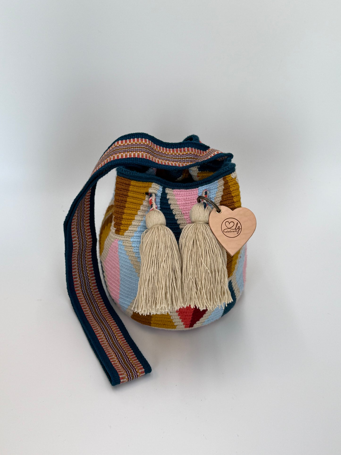 Voorkant van handgemaakte Wayuu tas Carmen Medium van LolaGrace met geometrisch patroon in blauw, roze en okergeel en crème kwastjes, artisan Wayuu bag uit Colombia.