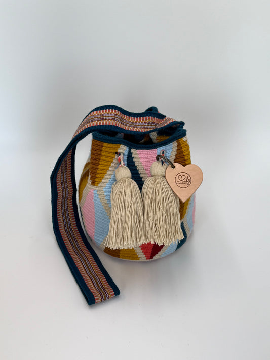 Voorkant van handgemaakte Wayuu tas Carmen Medium van LolaGrace met geometrisch patroon in blauw, roze en okergeel en crème kwastjes, artisan Wayuu bag uit Colombia.
