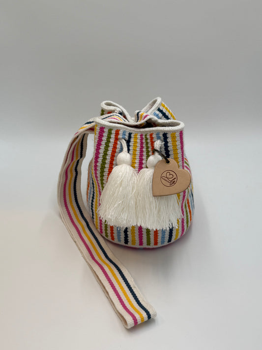 Voorkant van handgemaakte Wayuu tas Catalina Sofia Medium van LolaGrace met kleurrijke verticale strepen in roze, geel, blauw en groen en witte kwastjes.