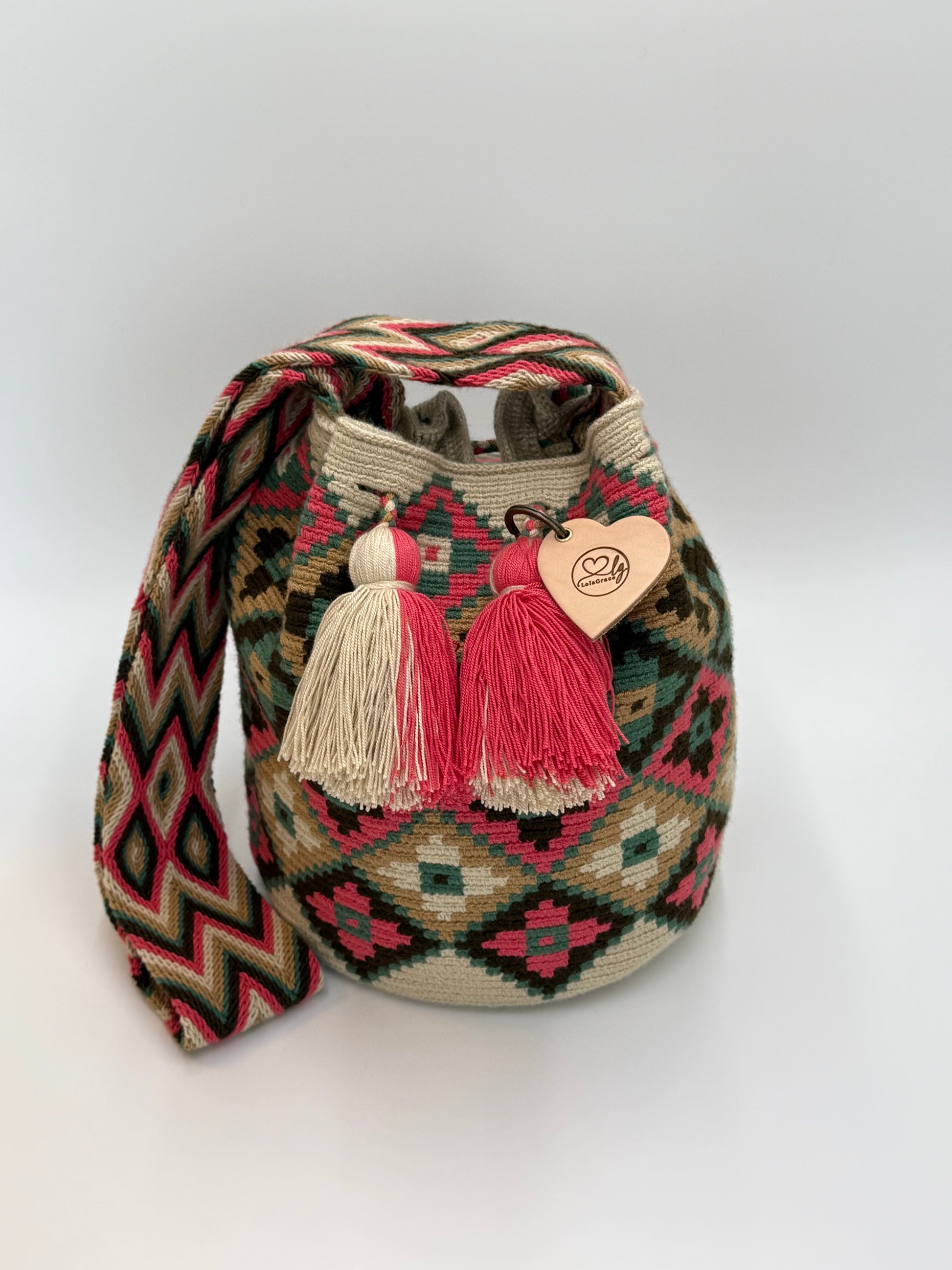 Voorkant van handgemaakte Wayuu tas Claudia Large van LolaGrace met geometrisch patroon in crème, groen, bruin en koraalroze en kwastjes in roze en beige.