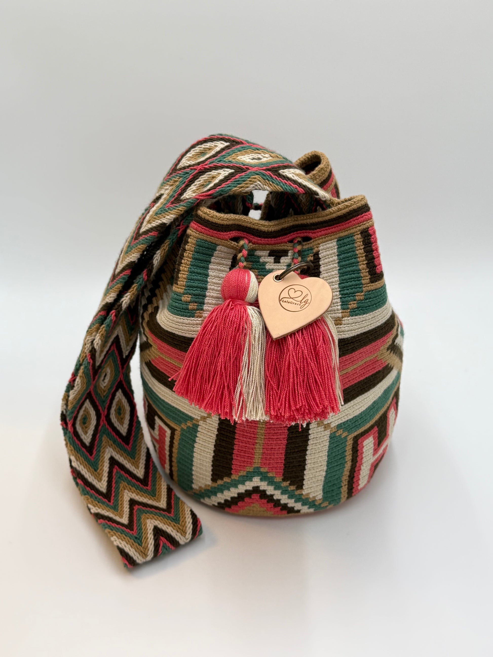 Voorkant van handgemaakte Wayuu tas Luz Elena Large van LolaGrace met geometrisch patroon in groen, crème, bruin en koraalroze en kwastjes in roze en beige.