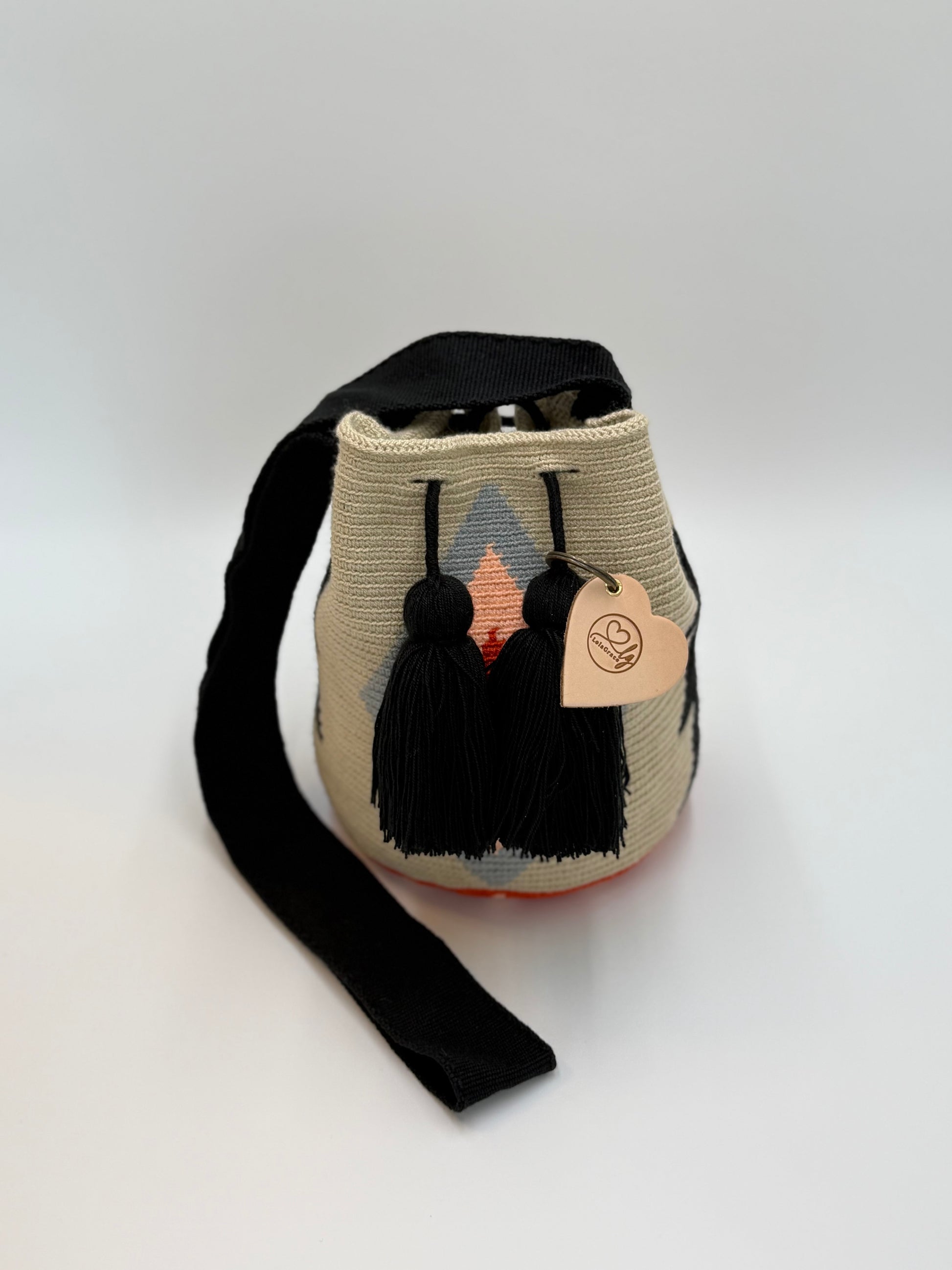 Medium Wayuu tas Nayibe in zandkleur met grafisch patroon in zwart, grijs en warme perziktinten, afgewerkt met zwarte kwastjes