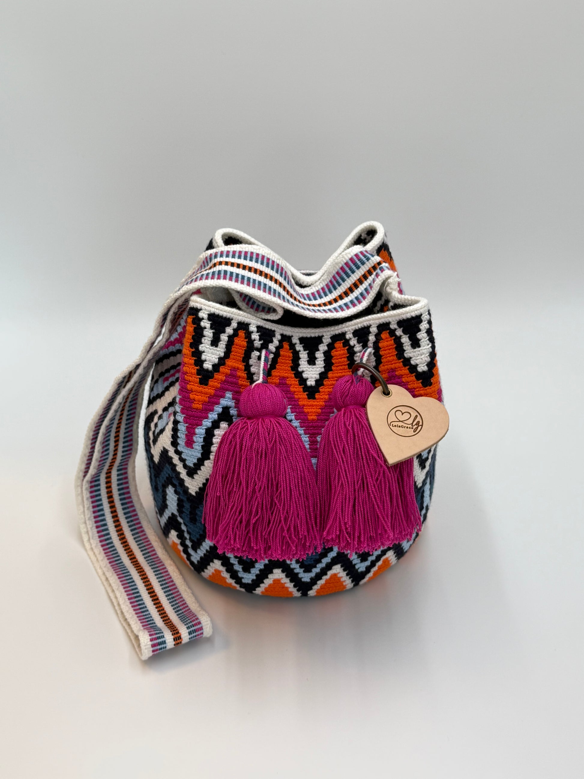 Rosaura Medium Wayuu mochila tas van LolaGrace, handgehaakt door de Wayuu gemeenschap in La Guajira, Colombia, met kleurrijk geometrisch patroon en fuchsia roze kwasten.