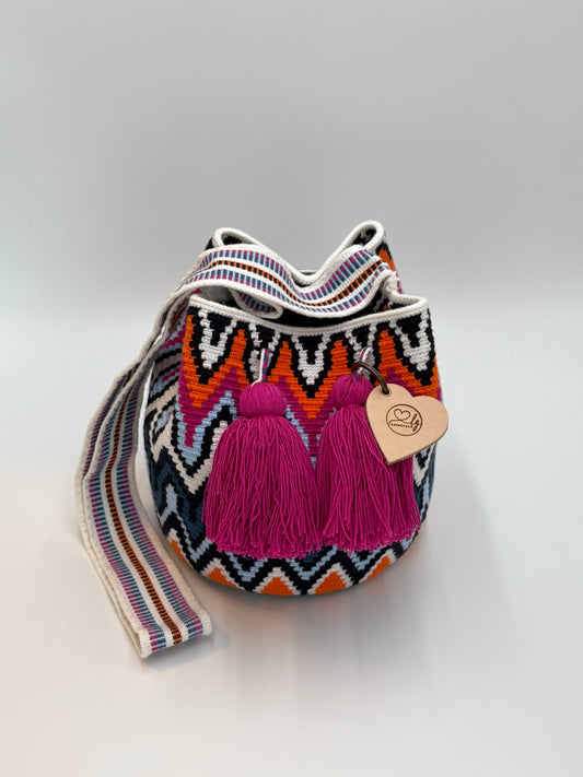 Rosaura Medium Wayuu mochila tas van LolaGrace, handgehaakt door de Wayuu gemeenschap in La Guajira, Colombia, met kleurrijk geometrisch patroon en fuchsia roze kwasten.